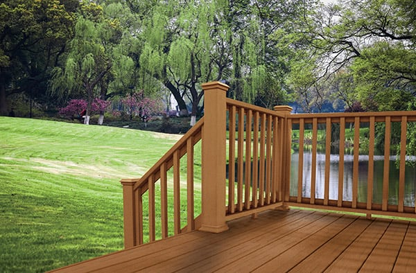  A composite wood deck railing and floor overlook a lush green park with trees and a small lake or pond in the background.